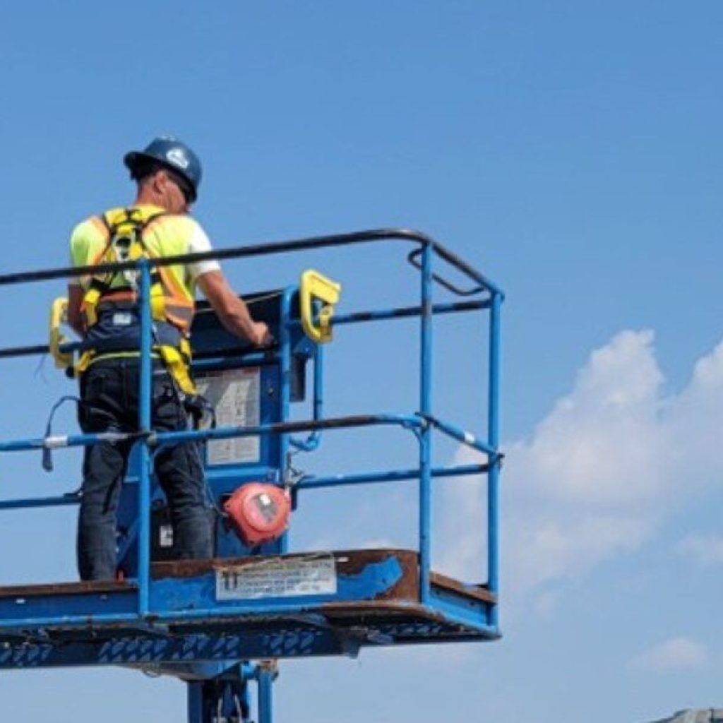 Operator working from the raised basket of a boom lift at a Manitoba worksite during on-site boom lift training