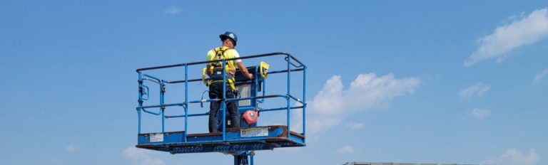 Operator working from the raised basket of a boom lift at a Manitoba worksite during on-site boom lift training
