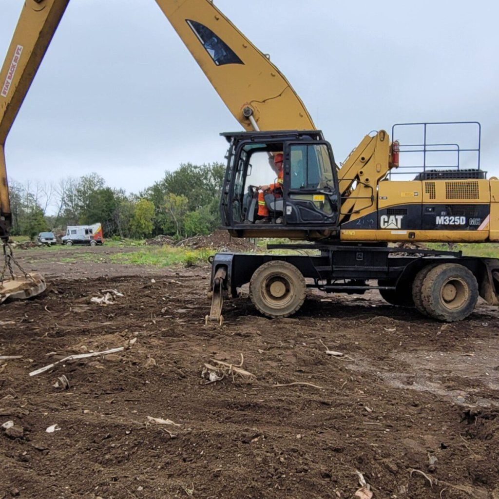 Operator working a wheeled excavator on cleared ground at a Manitoba site during on-site excavator training