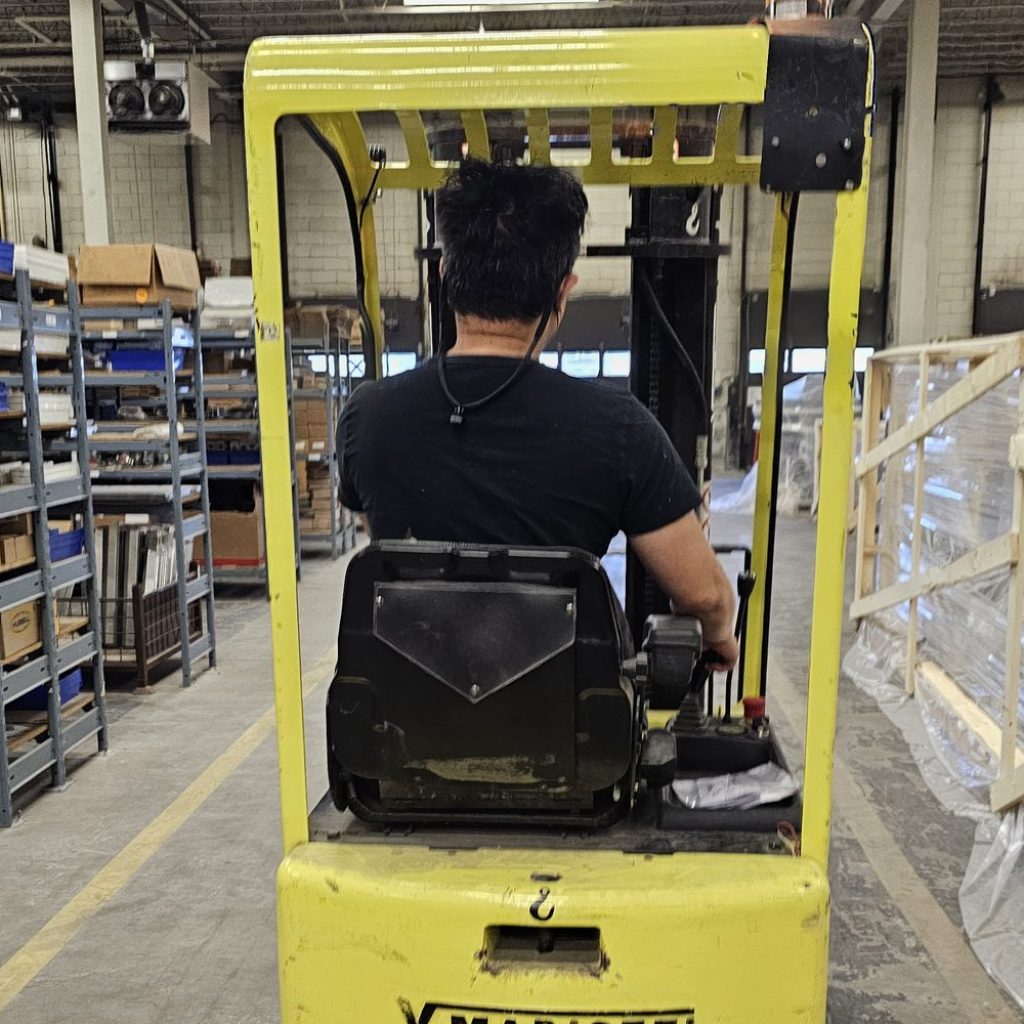 Operator seated on a sit-down counterbalance forklift in a warehouse aisle during a forklift train the trainer course in Winnipeg