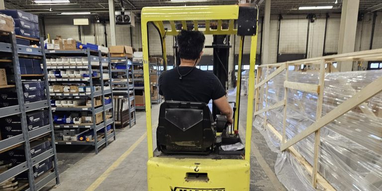 Operator seated on a sit-down counterbalance forklift in a warehouse aisle during a forklift train the trainer course in Winnipeg