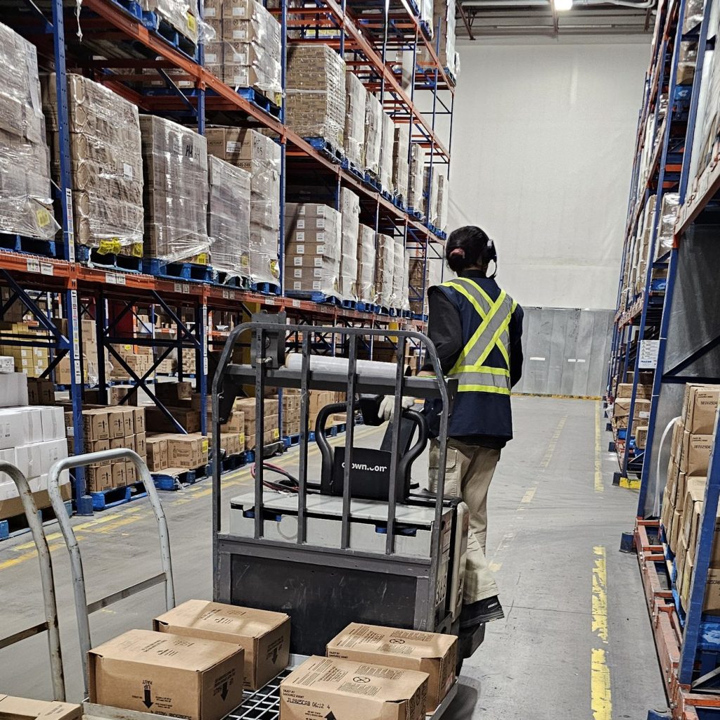 Operator in a hi-vis vest driving a loaded electric pallet jack down a warehouse aisle during pallet jack train the trainer in Winnipeg