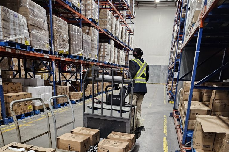 Operator in a hi-vis vest driving a loaded electric pallet jack down a warehouse aisle during pallet jack train the trainer in Winnipeg