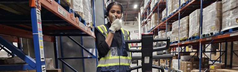 Warehouse worker in a hi-vis vest standing with an electric pallet jack during on-site pallet jack operator training in Winnipeg