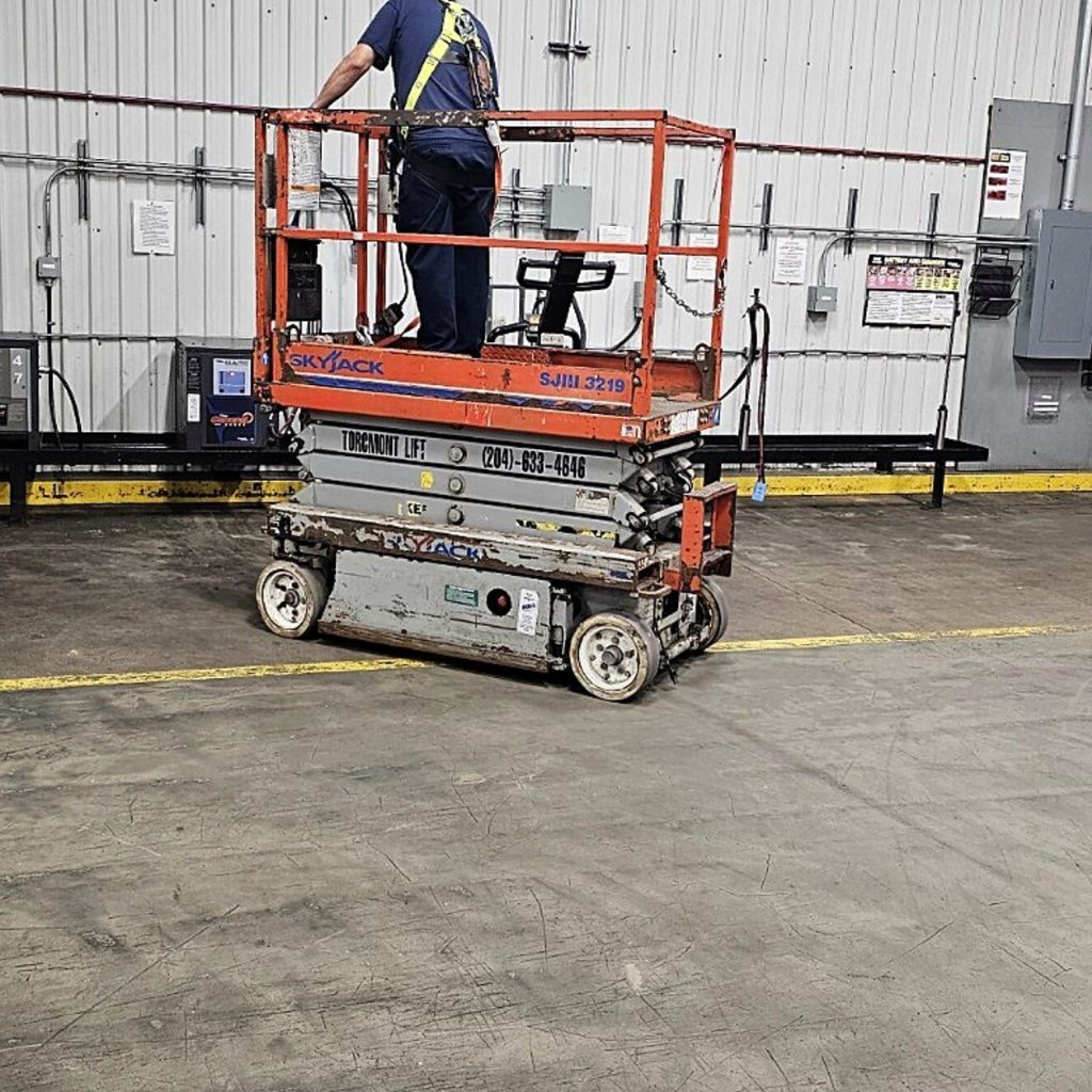 Worker on a raised scissor lift platform inside a building during on-site scissor lift training in Winnipeg