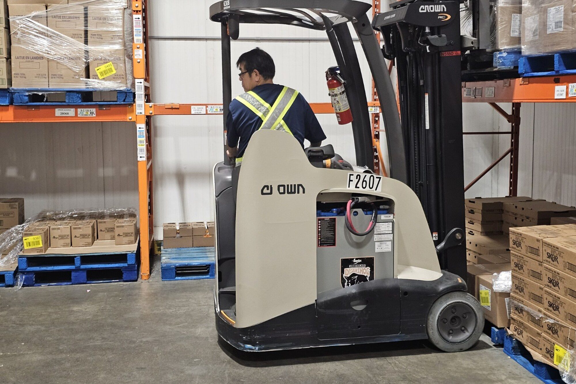 Operator in a hi-vis vest driving a stand-up reach truck down a warehouse aisle during on-site training in Winnipeg