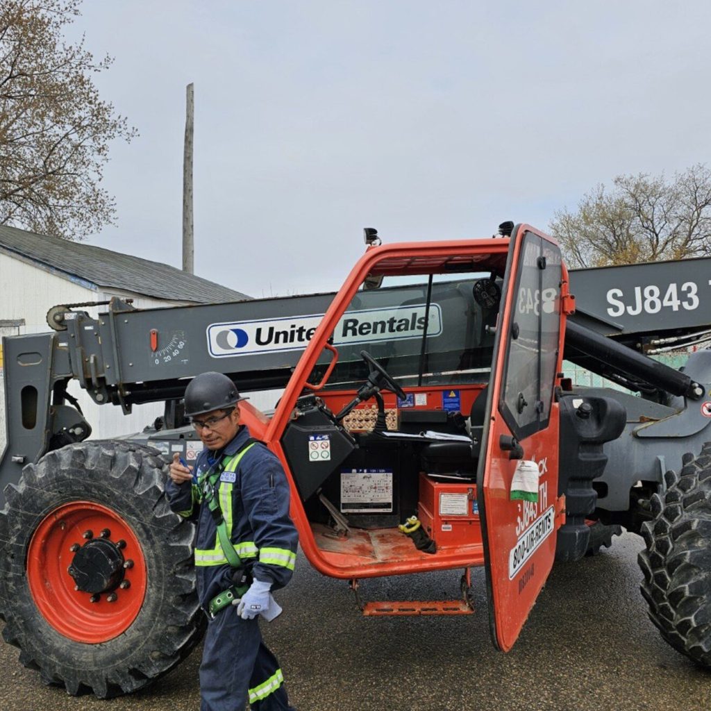 Worker standing beside a telehandler in a Winnipeg yard during a telehandler train the trainer course