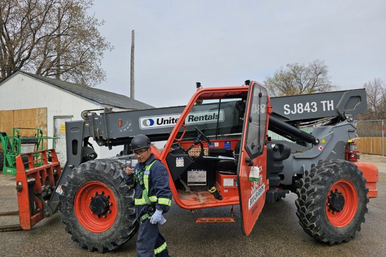 Worker standing beside a telehandler in a Winnipeg yard during a telehandler train the trainer course